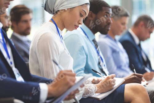 Preview: Side view of young mixed race businesswoman writing on notepad during seminar in office building