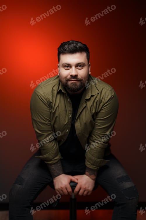 Preview: Cheerful bearded man on chair against red background