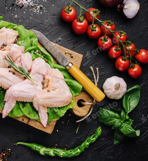Preview: Raw chicken wings with ingredients for cooking on a wooden cutting board over dark stone background