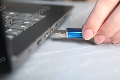 Preview: Woman inserting flash drive into laptop at gray table, closeup