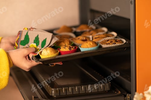 Preview: the girl takes out a baking sheet with freshly baked muffins from the oven