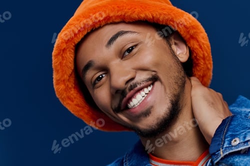 Preview: Young handsome man smiling brightly while wearing an orange hat against a deep blue backdrop