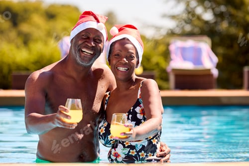 Preview: Portrait Of Senior Couple On Christmas Holiday In Swimming Pool Wearing Santa Hats