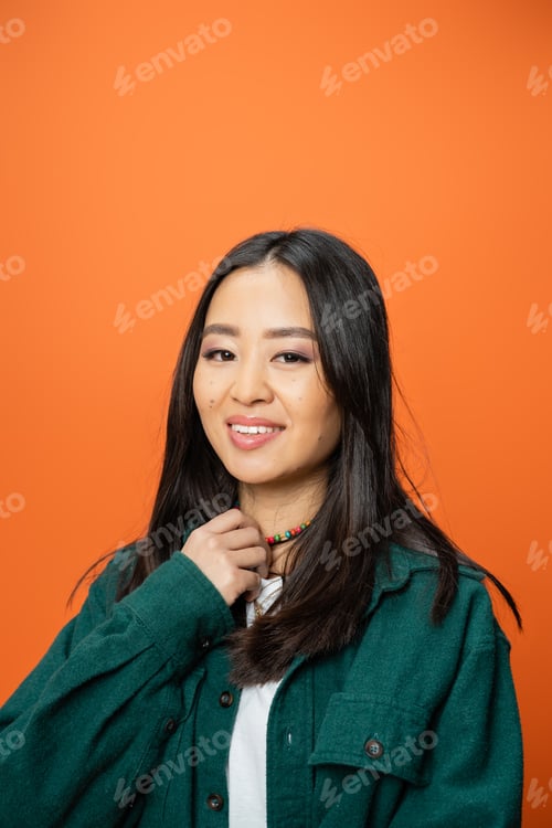 Preview: portrait of pretty asian woman in green shirt touching colorful beads and smiling at camera isolated