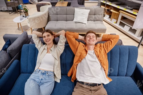 Preview: Relaxed couple sitting on sofa testing comfort of furniture at store