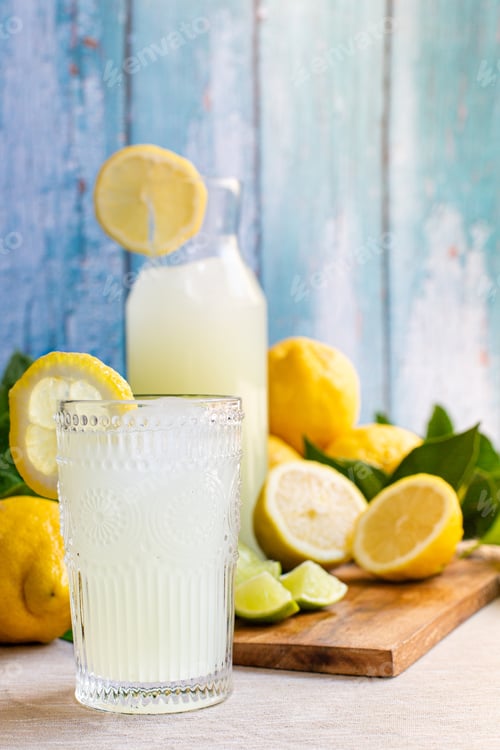 Preview: Vertical freshly squeezed lemon juice in a glass cup with lemons and lime on a wood board