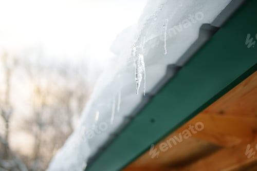 Preview: The roof of a house on a snowy winter day among thaw. Cleaning the roofing from snow and icicles.