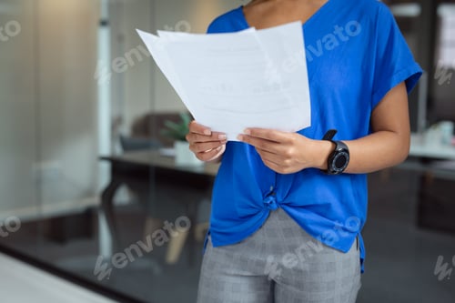 Preview: Midsection of african american businesswoman looking at paperwork standing in office