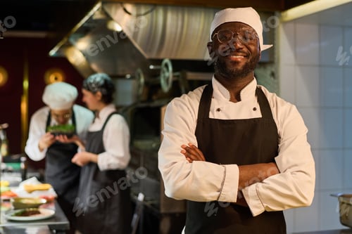 Preview: Happy African American male chef in uniform standing in front of camera