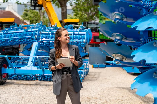 Preview: Smart casual businesswoman using digital tablet at agricultural equipment dealership