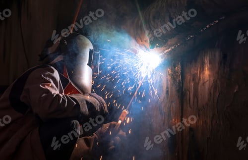 Preview: welder using arc welding machine to welding metal wall of the old vessel at shipyard in dark tone
