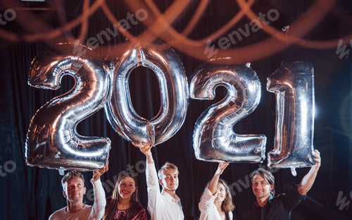 Preview: Cheerful group of people with drinks and balloons in hands celebrating new 2021 year