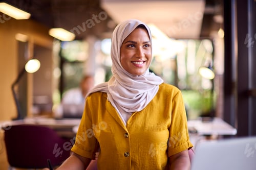 Preview: Mature Businesswoman Wearing Headscarf Working On Laptop At Desk In Office