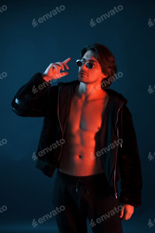 Preview: Beautiful man in glasses and black clothes is in the studio with blue neon lighting