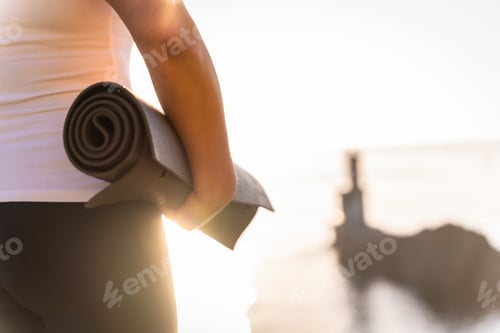 Preview: Hands of a woman with the yoga mat in nature by the sea at sunset, healthy and naturist life