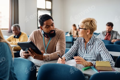 Preview: Black adult education teacher assisting mature student with her assignment during a class.