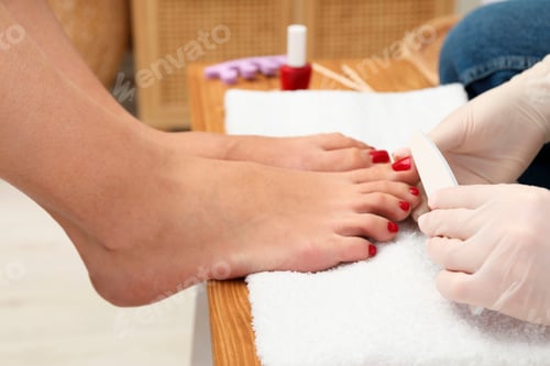 Preview: Pedicurist filing client`s toenails in beauty salon, closeup