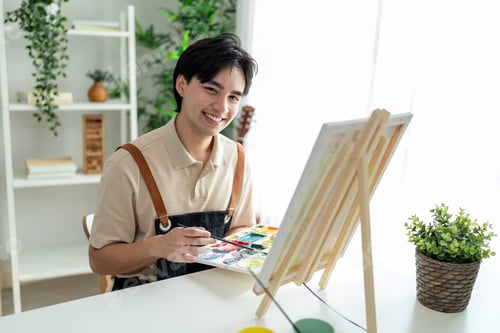 Preview: Portrait of Asian young talented man artist painting on board in house.