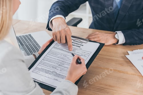 Preview: cropped view of businessman in blue jacket pointing on form for compensation claim with finger to