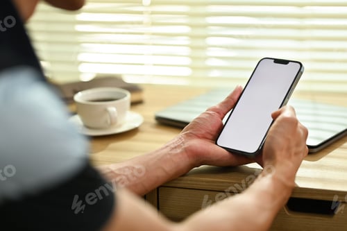 Preview: Young man hands holding smart phone with white empty screen sitting in cozy living room.