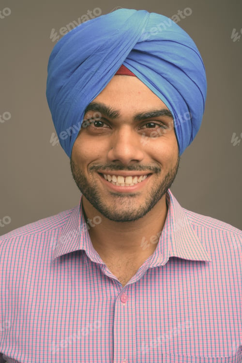 Preview: Young handsome Indian businessman wearing turban against gray background