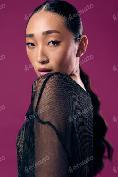 Preview: Asian woman with long hair wearing a sheer top posing against a purple background with hands on hips