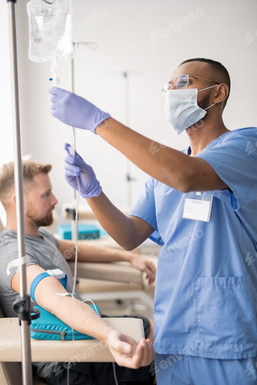 Preview: Young mixed-race doctor in uniform preparing dropper for patient in hospital