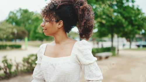 Preview: Smiling young woman walking in the park. Girl goes in the city park and looks at around