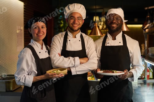 Preview: Group of young intercultural successful cooks in uniform looking at camera
