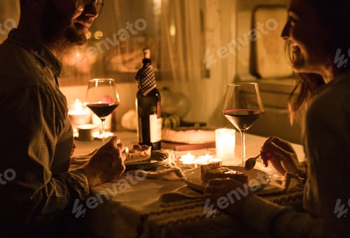 Preview: Couple having a lovely date by the candlelight, drinking red wine and serving dessert.