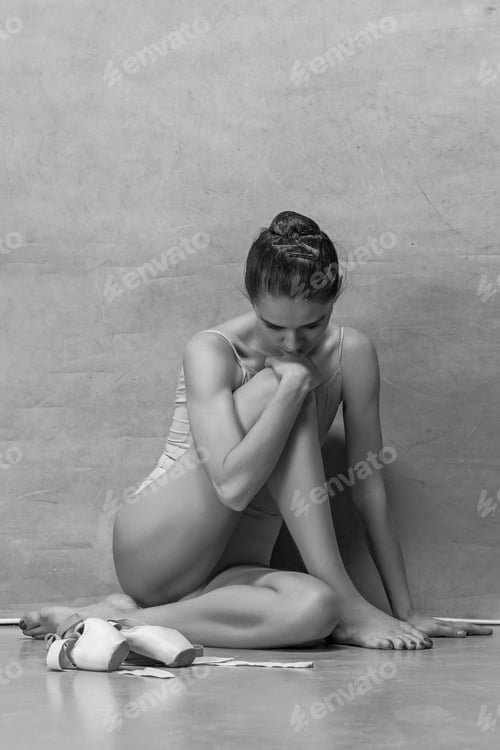 Preview: Tired ballet dancer sitting on the wooden floor on a pink background