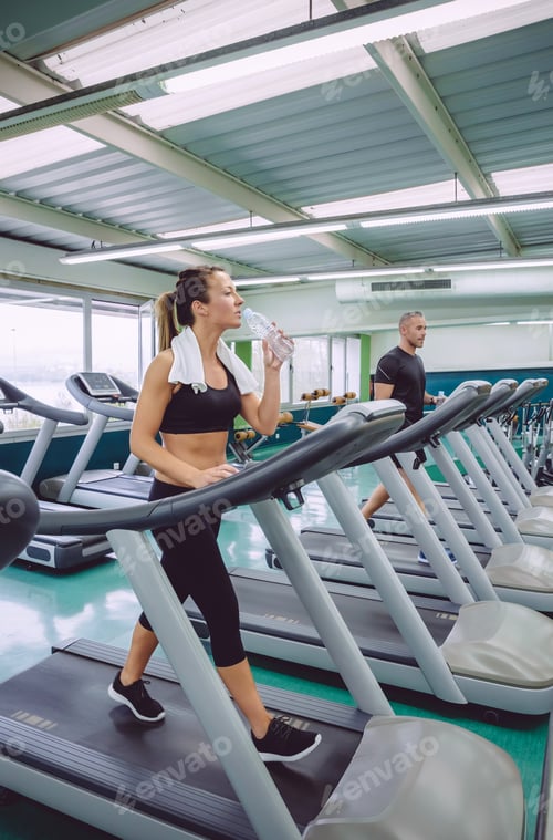 Preview: Woman drinking water while training on treadmill