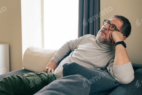 Preview: Senior man resting on sofa at home with thoughtful and mentally tired expression