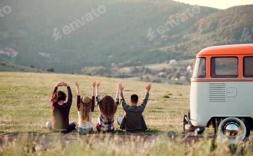 Preview: A rear view of group of young friends sitting on grass on a roadtrip through countryside.