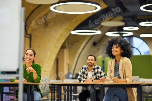 Preview: Group of young happy multiracial people sitting at desks in the modern office and listening to coach