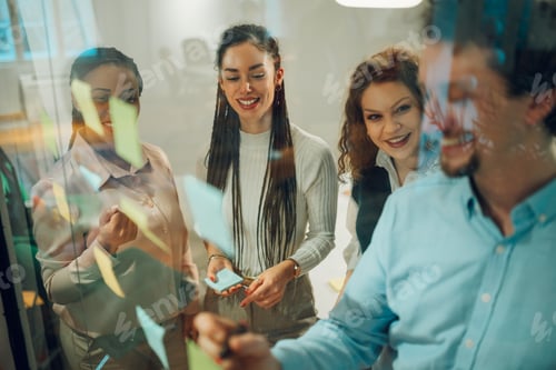 Preview: Businesspeople planning strategy using sticky notes on glass wall in office