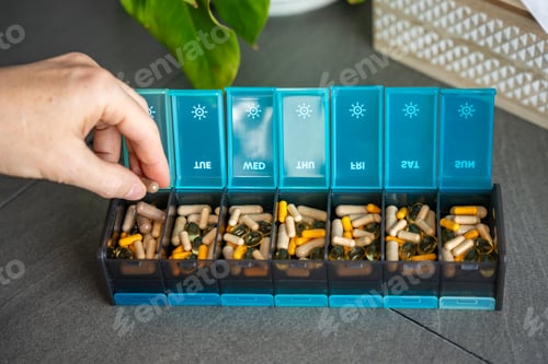 Preview: Man taking pills and supplements from his weekly pill organizer.