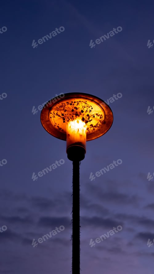 Preview: Vertical low angle shot of a glowing old street lamp under a blue sky