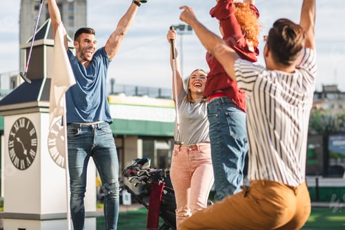Preview: Group of smiling friends enjoying together playing mini golf in the city.