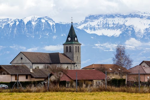 Preview: Dark contrast silhouette of church roof with tower against magnificent Alps mountains