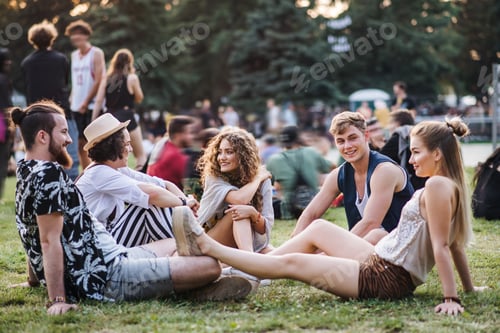 Preview: Group of young friends sitting on ground at summer festival