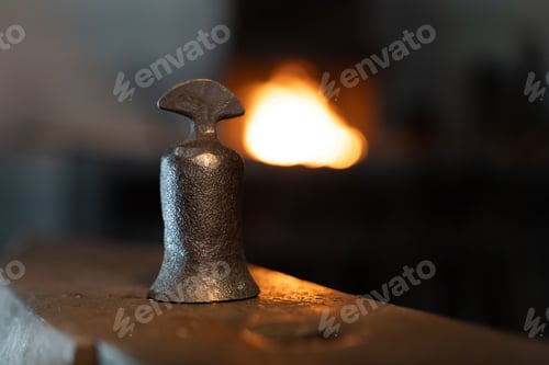 Preview: Closeup of an iron bell against a blurred view of a fire heating metals in a smithy