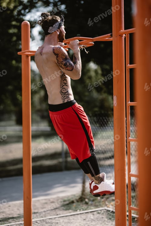 Preview: Young athletic man in headband with naked torso dressed in black leggings and red shorts pulls up on