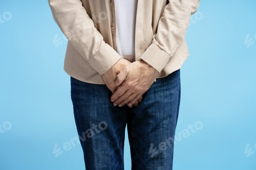 Preview: Senior man experiencing discomfort holding groin area on blue background