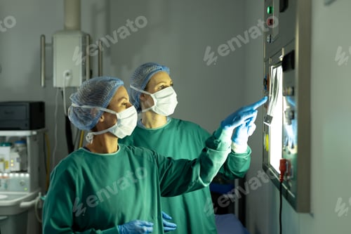Preview: Two diverse female surgeons preparing for operation, studying x-ray in operating theatre
