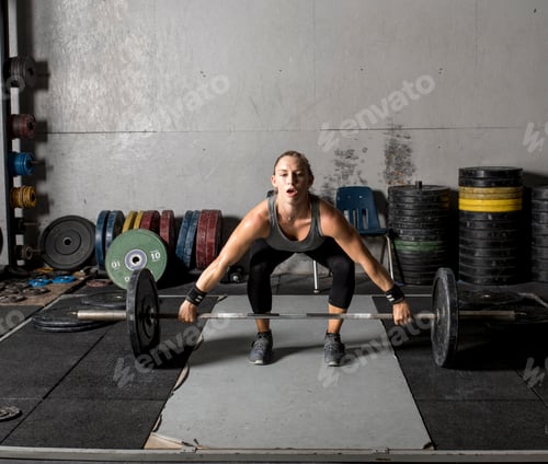Preview: Young strong woman lifting weights in gym.