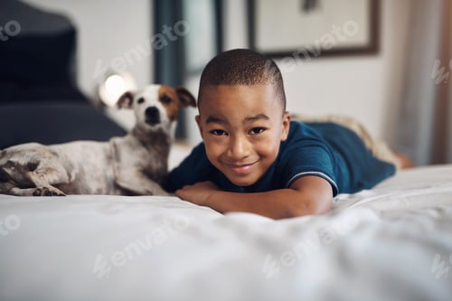 Preview: Shot of an adorable little boy playing with his pet dog on the bed at home