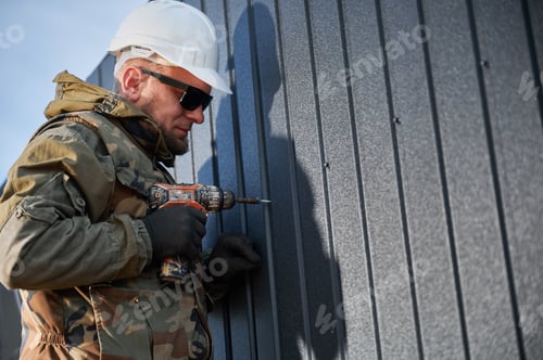 Preview: Builder installing corrugated iron sheet used as facade of future wooden frame house.