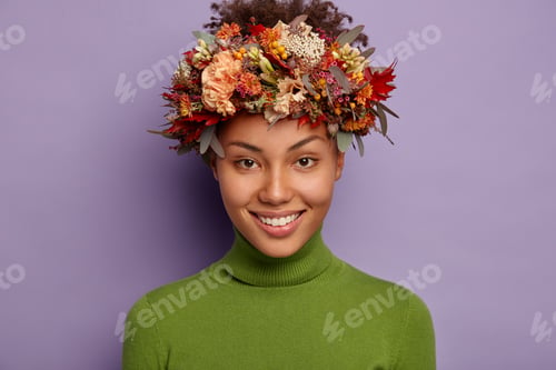 Preview: Portrait of pretty dark skinned female smiles pleasantly, wears beautiful wreath made of autumn attr
