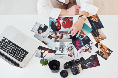Preview: Close up view of table with camera and photos. Female photographer at work